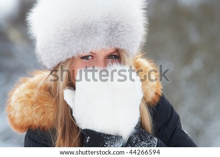 Young woman in fur-cap and fur mittens in winter forest