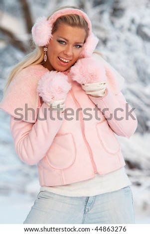 Funny teenage girl in rose coat and ear-flaps dancing in winter forest