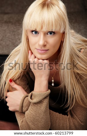 Portrait of beautiful happy lady with blue eyes in beige sweater sitting on a sofa