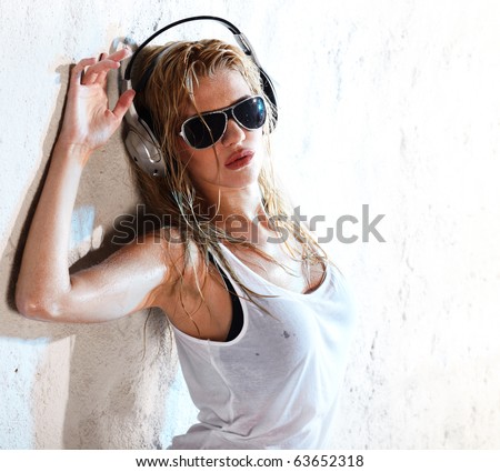 Wet babe in white shirt and sunglasses listening for the music using headphones