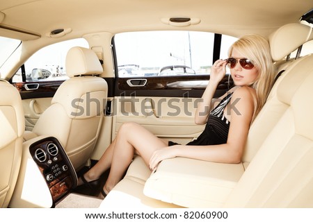 Young blond lady sitting on a backseat of a luxury car