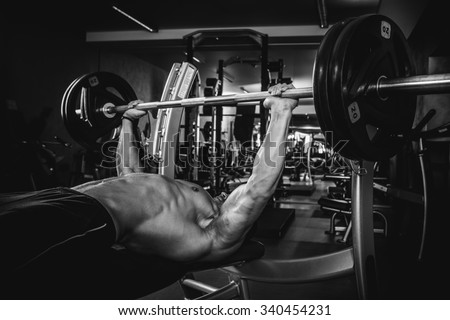 Brutal athletic man pumping up muscles on bench press in monochrome