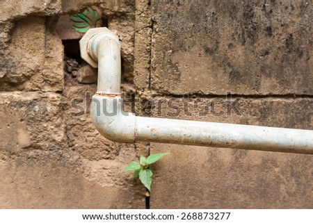 Metallic water pipe leading from an old brick-and-mortar wall