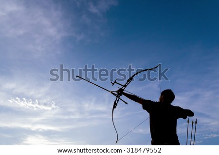 A silhouette of an archer drawing his bow and aiming upwards with deep blue sky and white clouds as background