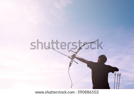 A silhouette of an archer drawing his bow and aiming towards white light with soft photo filter applied