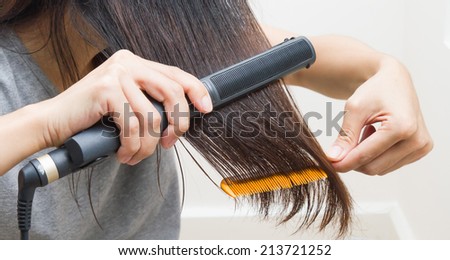 Woman straightening hair with straightener on right hand and comb on left hand.