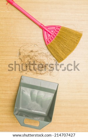 Dirty alopecia hair on laminate floor with broom and dustpan.