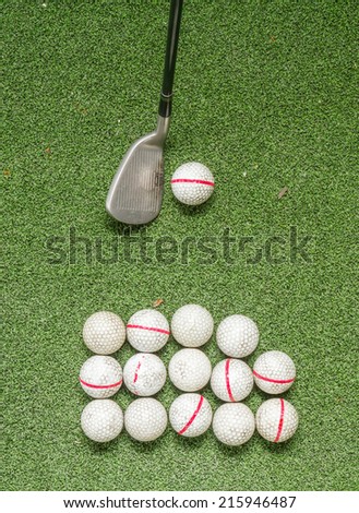 Old golf balls and iron on artificial grass in driving range for swing practice.