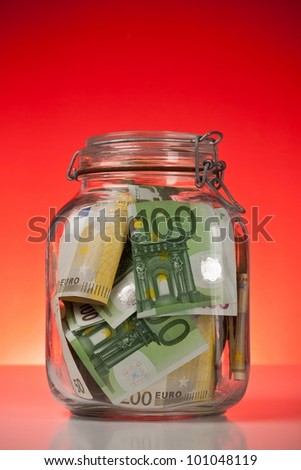 Glass bank for tips with money on red background