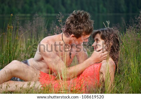 Young couple sitting on the grass on the shore, lost in love