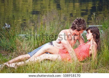 Young couple lost in love lying on the grass on the shore