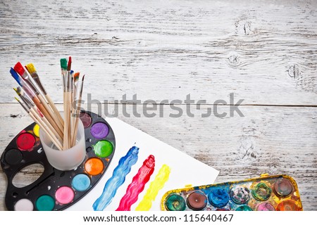 Box of watercolors and paintbrushes on wooden desk