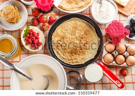 Frying pan with pancake and pancake ingredients on kitchen table