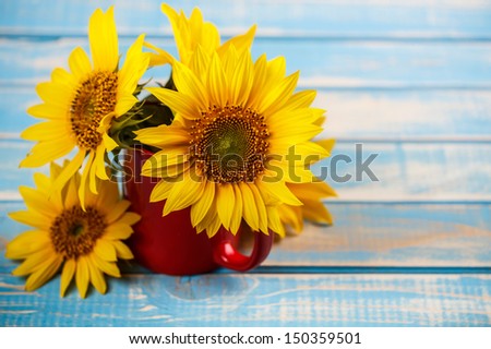 Sunflowers in red cup on blue board