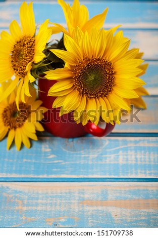 Sunflowers in red cup on blue board