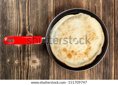 Frying pan with pancake on rustic wooden background