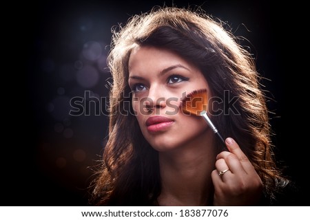 Young woman removing excess of powder using fan brush
