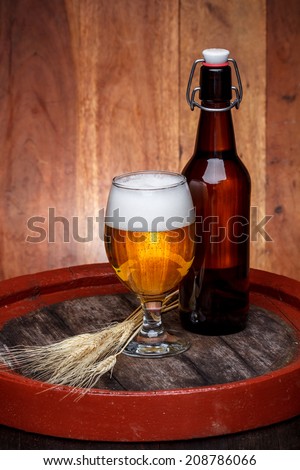 Glass of fresh beer with bottle on wooden barrel