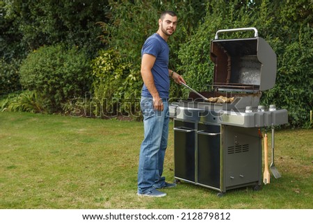 Handsome young man cooking meat for barbecue party in the garden