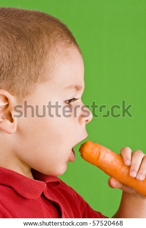 Boy eating fresh carrot isolated on green background