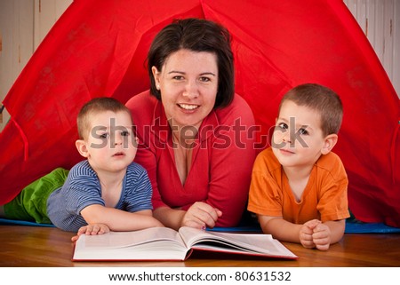 Mother with two young children lying in colorful tent and reading a book