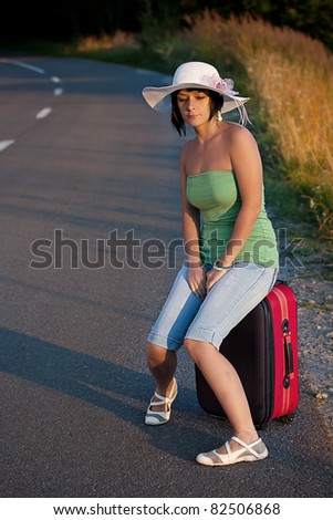 Beautiful woman sitting on a suitcase by a countryside road