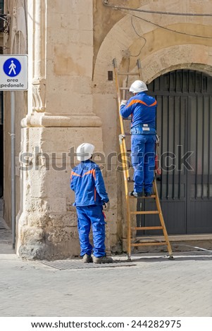 Syracuse, Italy, November 2014: Two workers of the Italian electricity company trying to repair a fault in the narrow streets of Syracuse
