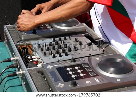 A closeup of a pair of hands mixing music on a DJ deck out in the open sunlight