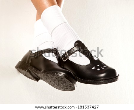 A dangling set of kids legs with short white socks and black girls school shoes on a white background