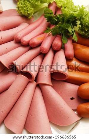 A collection of cold meats, bologna, and vienna sausages garnished with parsley and tomato on an isolated white studio background