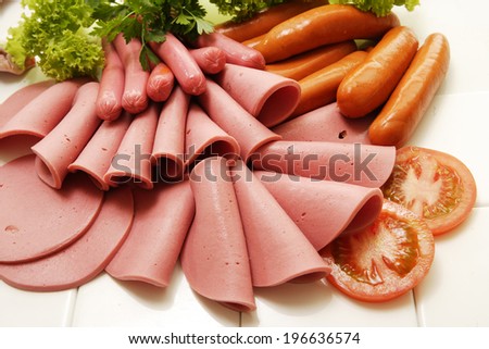 A collection of cold meats, bologna, and vienna sausages garnished with parsley and tomato on an isolated white studio background