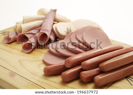 A collection of cold meats, bologna, and vienna sausages on a wooden board on an isolated white studio background