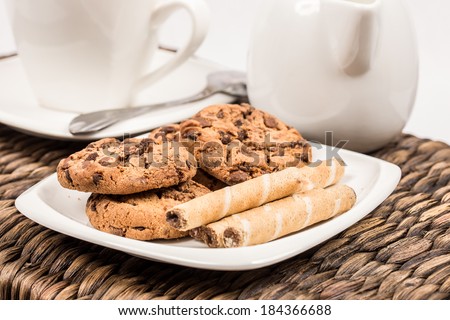 chocolate cookies and wafer roll with hazelnut creme next to cup of coffee   on the wicker background