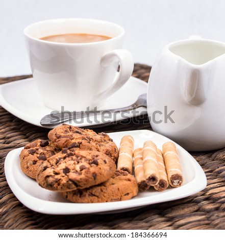 coffee with chocolate cookies and wafer roll with hazelnut creme on the wicker background