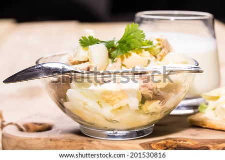 Fish, egg, vegetables salad in the bowl and garlic souse on the wooden table