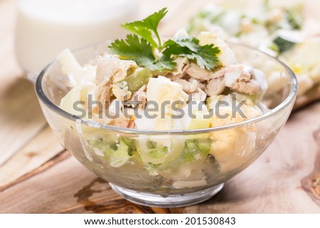 Fish, egg, vegetables salad in the bowl and garlic souse on the wooden table