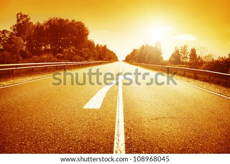 Country road with arrow sign on asphalt and sunset.