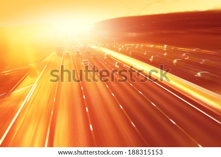 Cars in motion blur on highway during sunset.