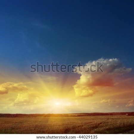Sunset sky with rays of light over field.