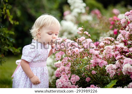 Baby girl in pink dress smell flavor of roses in the garden full of flowers