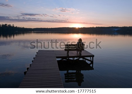 person sitting on dock on calm lake at sunset