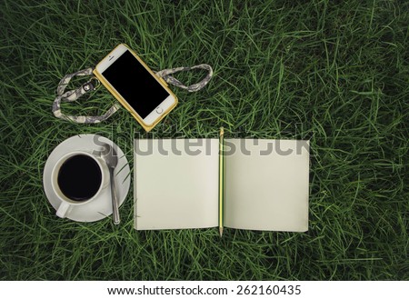 Pencil ,notebook ,white cup of hot coffee and smart phone on the grass ,Still life