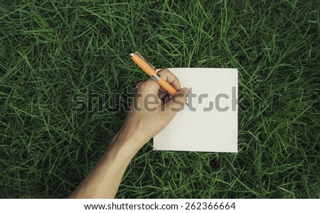 Close up of a hand writing on a notebook outdoor lying on the grass in a park