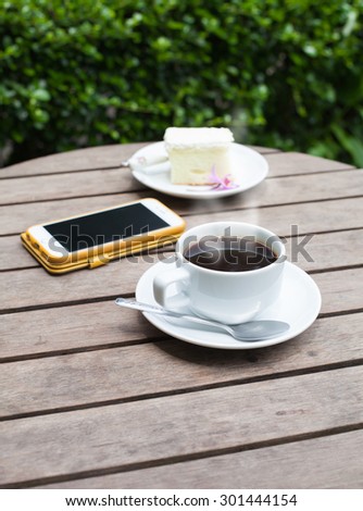 Black coffee phone and cakes on a wooden table in the garden, soft focus