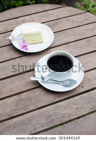 Black coffee and cakes on a wooden table in the garden, soft focus for background.