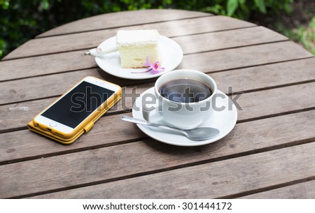 Black coffee phone and cakes on a wooden table in the garden, soft focus