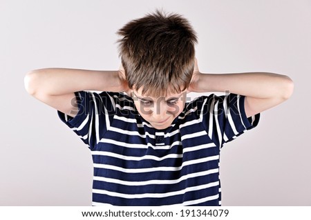 Young boy bending his head and covering ears with hands because of loud noise