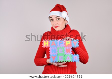 Woman in red with Santa hat holding a Happy New Year sign made of alphabet puzzle pieces