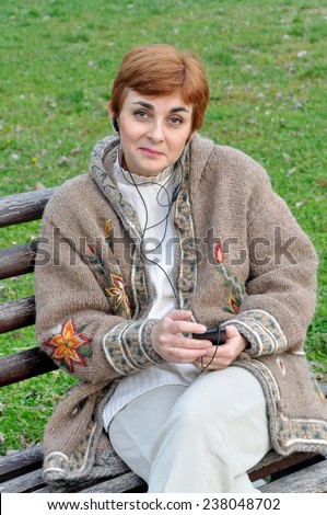 Woman listening to music and sitting on the bench in the city park