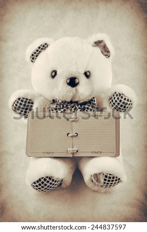 Teddy bear holding a small old blank notepad isolated on brown background. Vintage style photo